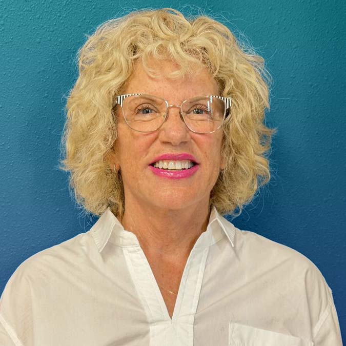 Smiling older woman with curly blonde hair, glasses; a counseling expert at Goodman's Behavioral Health.