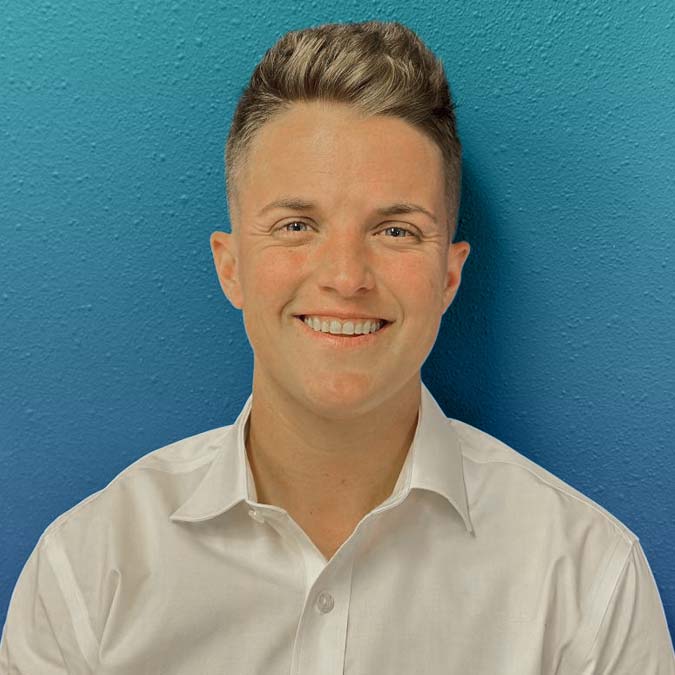 Smiling person with short hair in a white shirt, standing by a blue wall after counseling.