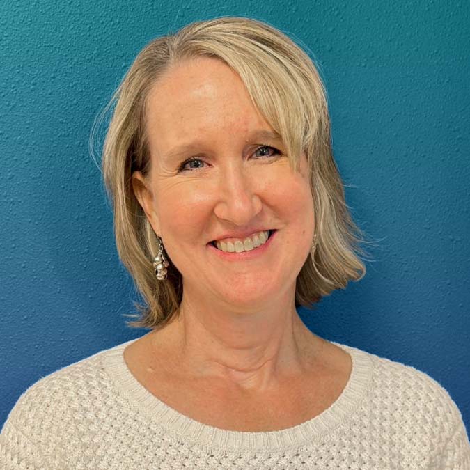 Smiling woman with short blonde hair, in a white sweater, at Goodman's Behavioral Health center.